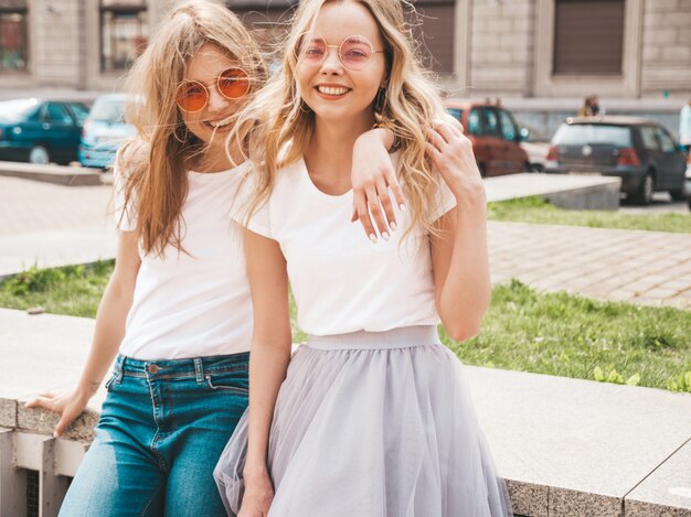 Retrato de dos jóvenes hermosas rubias sonrientes chicas hipster en ropa de moda verano camiseta blanca. .