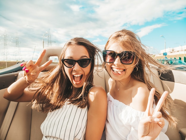 Retrato de dos jóvenes hermosas y sonrientes chicas hipster en coche descapotable