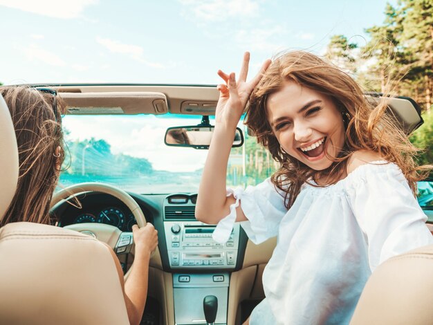 Retrato de dos jóvenes hermosas y sonrientes chicas hipster en coche descapotable