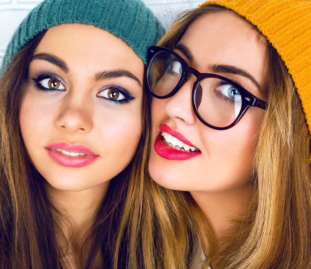 Retrato de dos muchachas bonitas con maquillaje brillante, sombreros y gafas