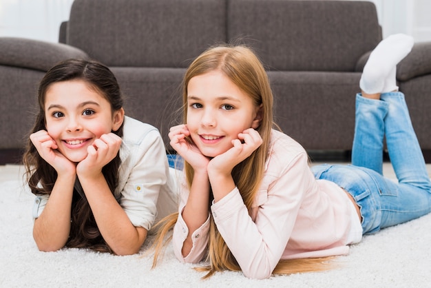 Retrato de dos muchachas felices que mienten en la alfombra blanca delante del sofá