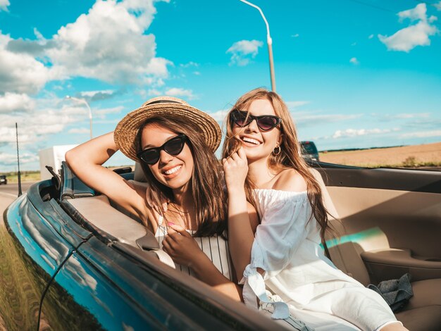 Retrato de dos mujeres hipster hermosa y sonriente joven en coche descapotable