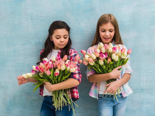 Retrato de dos niñas de pie frente a una pared azul con ramo de flores de tulipán