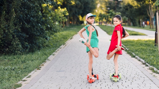 Retrato de dos niñas de pie sobre una pierna sobre el patinete en el parque