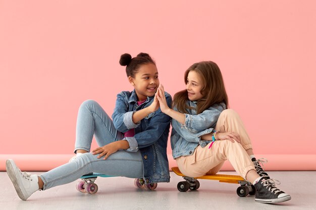 Retrato de dos niñas sonrientes choca los cinco en patinetas