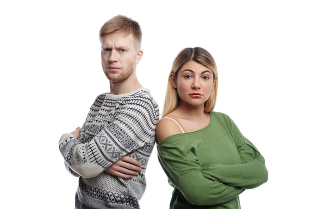 Retrato de dos padres jóvenes, hombres y mujeres, de apariencia caucásica de pie con los brazos cruzados, mirando con enojo, disgustado con el mal comportamiento de su pequeño hijo