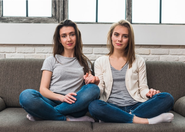 Retrato de dos parejas de lesbianas jóvenes sentados en un sofá con las piernas cruzadas mirando a la cámara