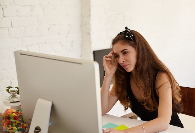 Retrato de economista mujer caucásica está analizando las actividades de la empresa a través de PC sentado frente a la computadora en la oficina. Joven emprendedora trabajando duro para lograr los objetivos empresariales