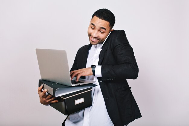 Retrato elegante alegre guapo ocupado en camisa blanca y chaqueta negra sosteniendo carpetas, portátil, hablando por teléfono. Hombre de negocios, gran éxito, sonriendo, ocupado, ocupación.