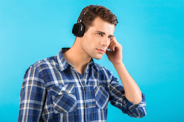 Retrato de elegante atractivo joven guapo escuchando música en auriculares inalámbricos divirtiéndose estilo moderno feliz estado de ánimo emocional aislado sobre fondo azul con camisa a cuadros