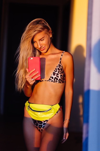 Retrato elegante colorido brillante de la mujer blogger delgada en forma joven en bikini leopardo en la cálida luz del atardecer tomar una foto