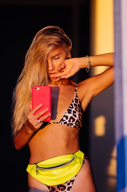 Retrato elegante colorido brillante de la mujer blogger delgada en forma joven en bikini leopardo en la cálida luz del atardecer tomar una foto