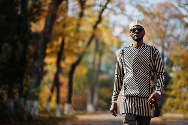 Retrato de un elegante hombre afroamericano negro con sombrero y gafas de sol contra el fondo soleado de otoño Gente rica en África con vestimenta tradicional