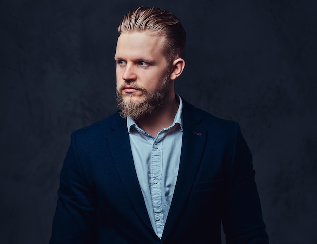 Retrato de un elegante hombre barbudo rubio vestido con un traje sobre fondo gris.