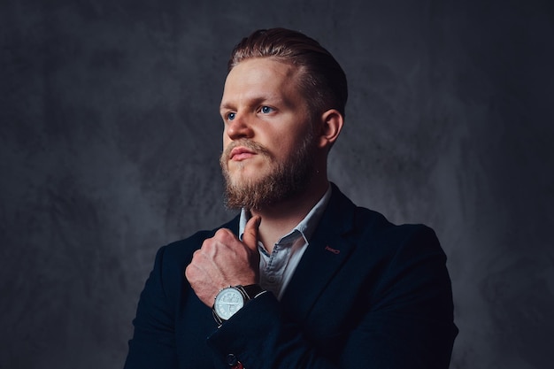 Retrato de un elegante hombre barbudo rubio vestido con un traje sobre fondo gris.