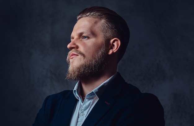 Retrato de un elegante hombre barbudo rubio vestido con un traje sobre fondo gris.