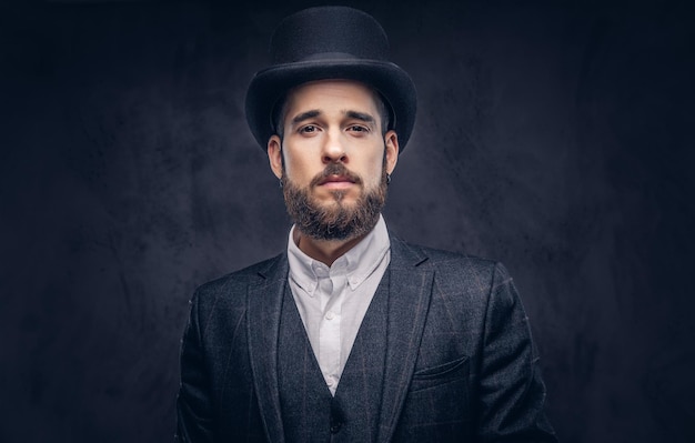 Retrato de un elegante hombre barbudo con un traje elegante y un sombrero cilíndrico, mirando una cámara sobre un fondo oscuro.