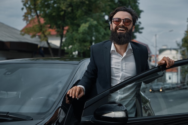 Retrato elegante, hombre guapo cerca del coche al aire libre