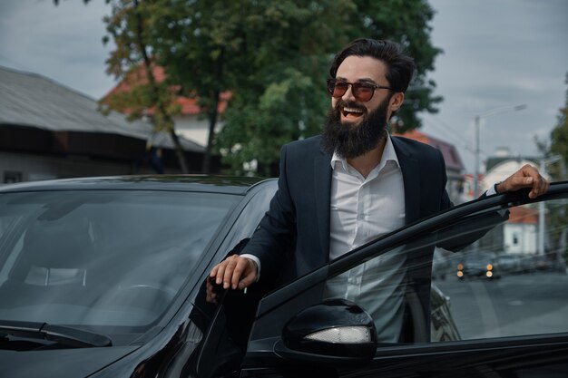 Retrato elegante, hombre guapo cerca del coche al aire libre