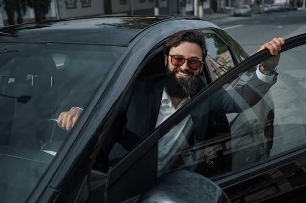 Retrato elegante, hombre guapo cerca del coche al aire libre