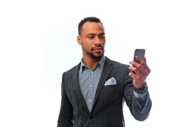 Retrato de un elegante hombre negro americano barbudo con traje que sostiene un teléfono inteligente. Aislado sobre fondo blanco.