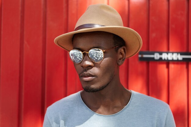 Retrato de elegante joven afroamericano guapo con cerdas de pie al aire libre contra la pared roja