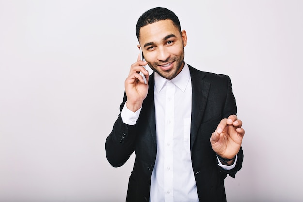 Retrato elegante joven guapo en camisa blanca, chaqueta negra hablando por teléfono y sonriendo. Logra el éxito, expresando verdaderas emociones positivas, empresario.