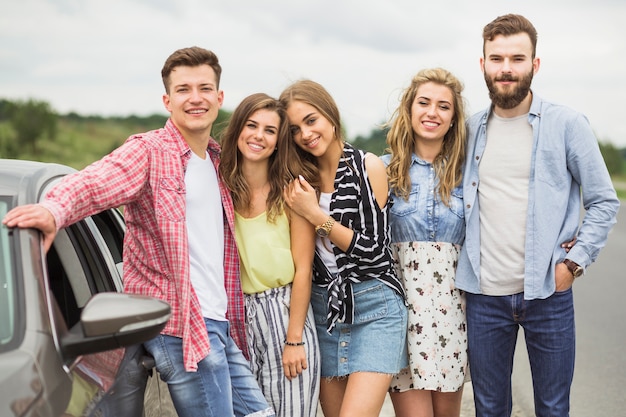 Retrato de elegantes jóvenes amigos posando cerca del coche estacionado