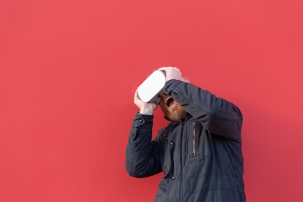 Retrato emocional de un hombre en la calle con gafas de realidad con el telón de fondo de una pared roja