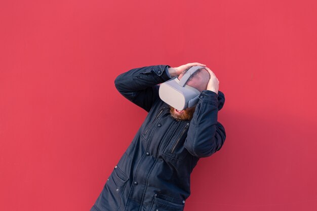 Retrato emocional de un hombre en la calle con gafas de realidad con el telón de fondo de una pared roja