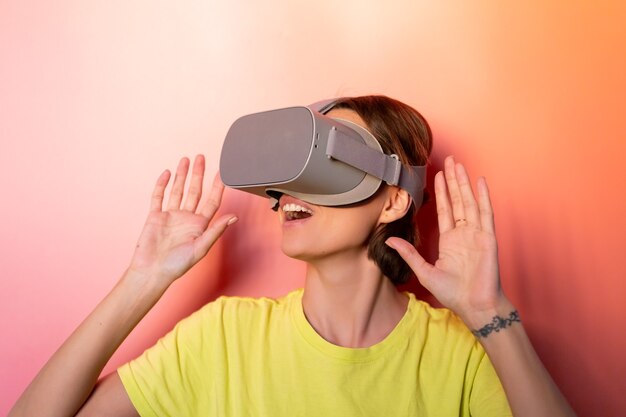 Retrato emocional de mujer con gafas de realidad virtual en estudio sobre fondo naranja rosa