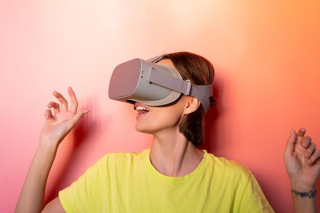 Retrato emocional de mujer con gafas de realidad virtual en estudio sobre fondo naranja rosa