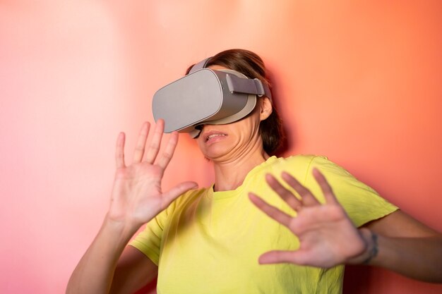 Retrato emocional de mujer con gafas de realidad virtual en estudio sobre fondo naranja rosa