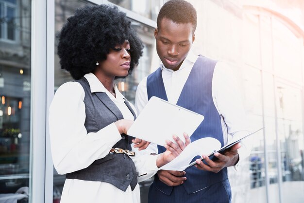 Retrato de una empresaria africana joven que muestra algo en la tableta digital a su colega