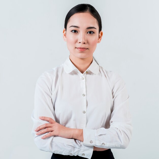 El retrato de una empresaria asiática joven con su brazo cruzó la mirada a la cámara aislada en el fondo blanco