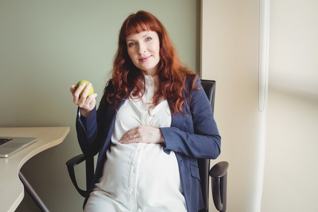 Retrato de empresaria embarazada sosteniendo una manzana