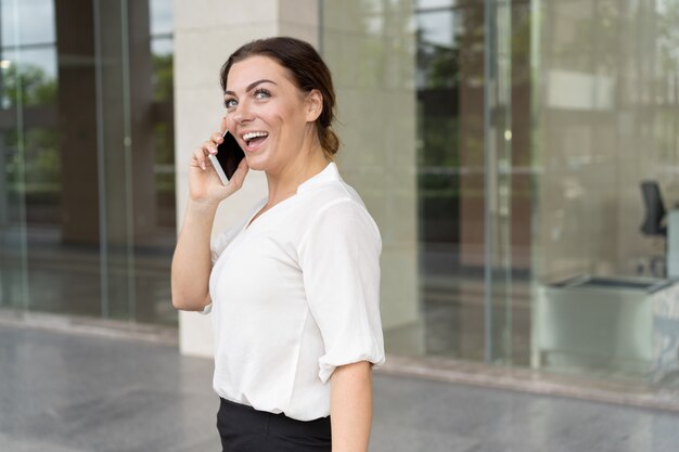 Retrato de empresaria excitada hablando por teléfono inteligente al aire libre