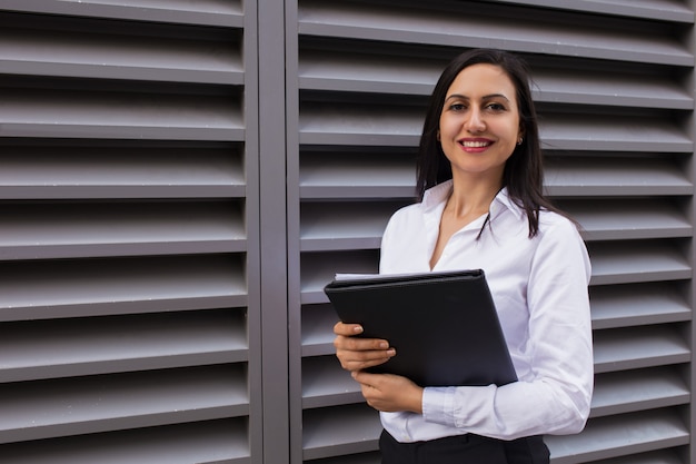 Retrato de la empresaria joven acertada que se coloca con la carpeta