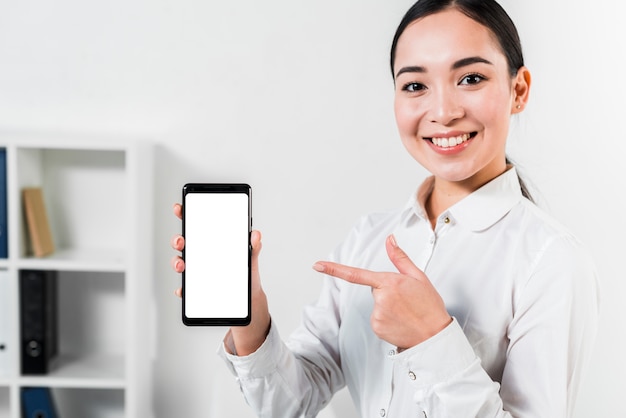 Retrato de una empresaria joven asiática feliz que señala en el teléfono móvil