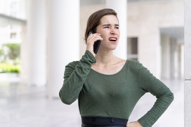 Retrato de la empresaria joven enojada que habla en el teléfono móvil