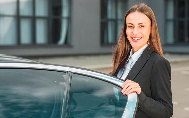 Retrato de una empresaria joven feliz que se coloca cerca de puerta de coche abierta