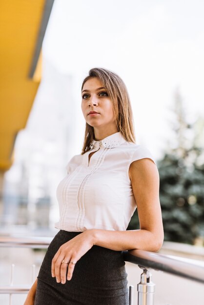 Retrato de la empresaria joven moderna que se coloca cerca de la verja que mira lejos