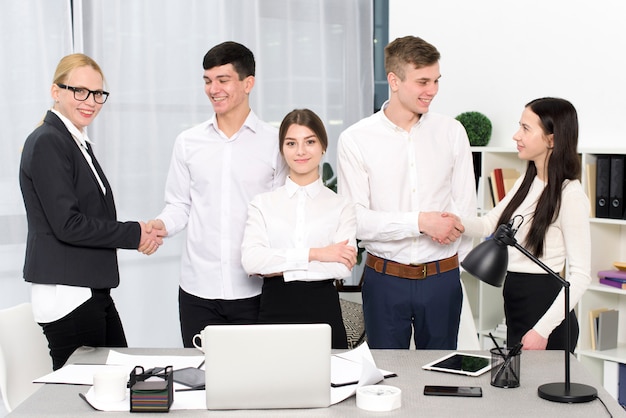 Foto gratuita retrato de una empresaria joven que se coloca con los hombres de negocios que sacuden las manos de cada uno en el lugar de trabajo