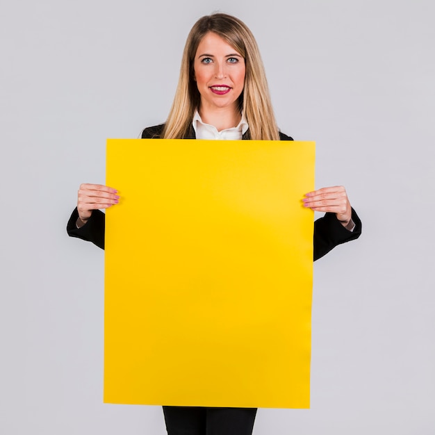Retrato de una empresaria joven que muestra el cartel amarillo en blanco en fondo gris