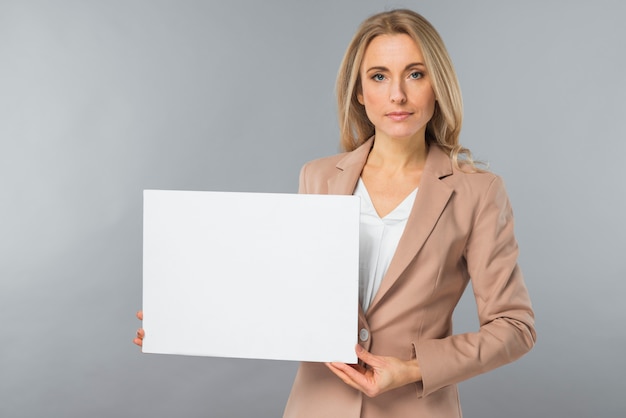 Retrato de la empresaria joven que muestra el cartel blanco en blanco contra fondo gris