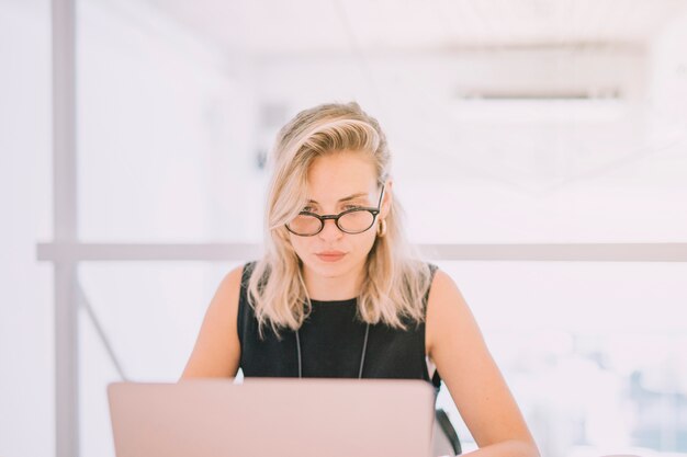 Retrato de la empresaria joven rubia que mira la computadora portátil