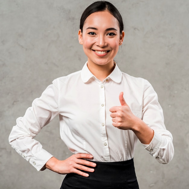 Foto gratuita retrato de una empresaria joven sonriente con la mano en sus caderas que muestran el pulgar encima de la muestra