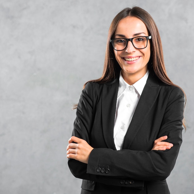 Retrato de una empresaria joven sonriente de pie con su brazo cruzado contra la pared gris