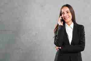 Foto gratuita retrato de una empresaria joven sonriente que escucha en smartphone contra fondo gris