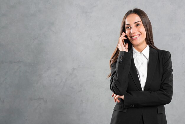 Retrato de una empresaria joven sonriente que escucha en smartphone contra fondo gris